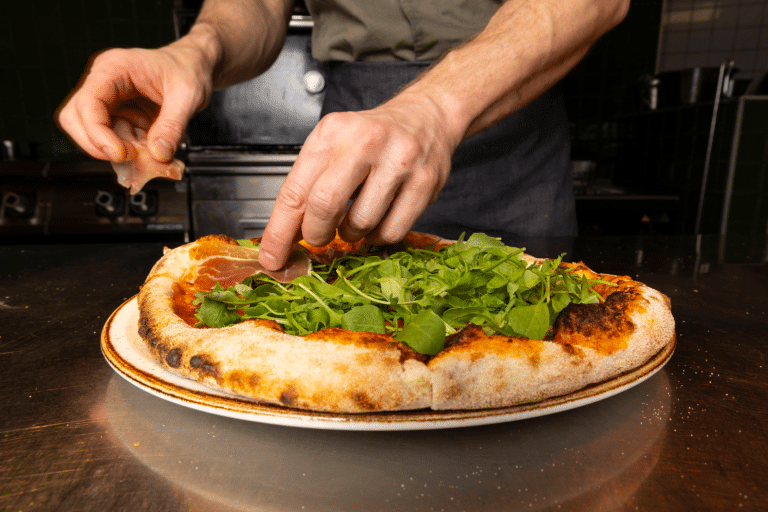 Øya Spiseri Porsgrunn – kokk som tilbereder italiensk-inspirert pizza med ruccola og spekeskinke.