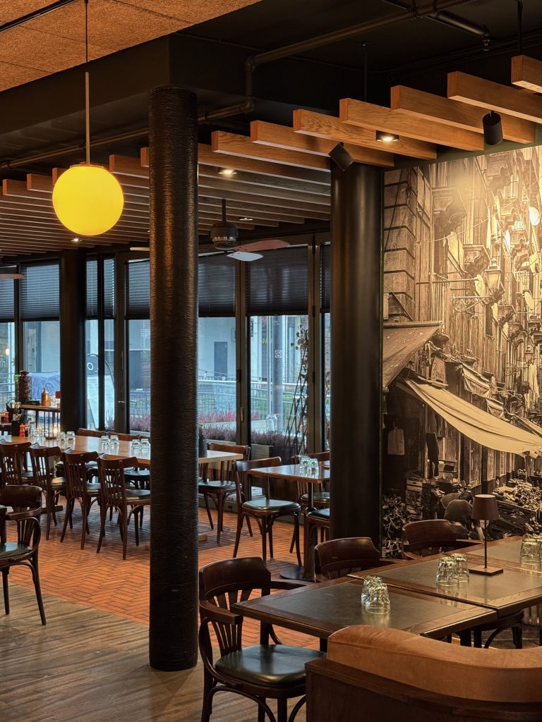 Øya Spiseri Porsgrunn – innbydende restaurantinteriør med tremøbler, gul belysning, store vinduer og stemningsfull italiensk veggkunst.