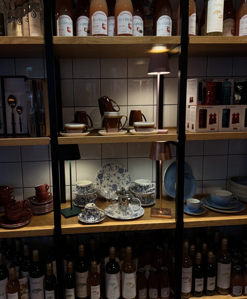 Hylleutstilling hos Øya Spiseri i Porsgrunn med serviser, kjøkkenartikler og vinflasker.